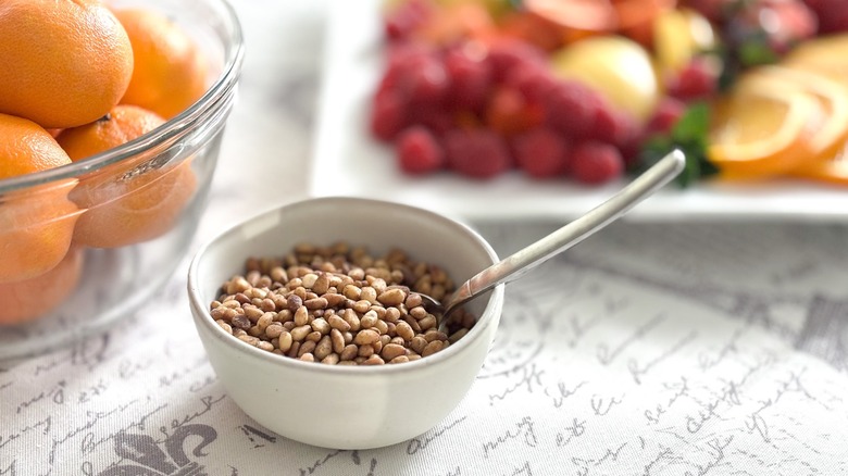 bowl of toasted pine nuts with fruit in background