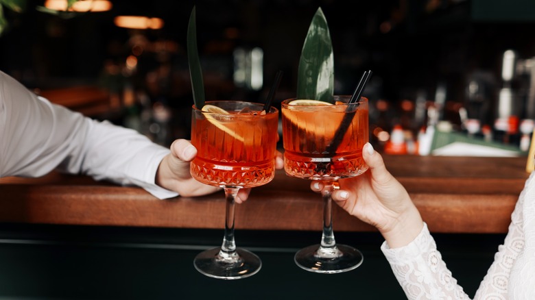 Two people toast Aperol spritz cocktail glasses