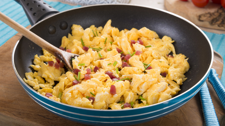 Eggs with bacon and herbs being scrambled in a skillet