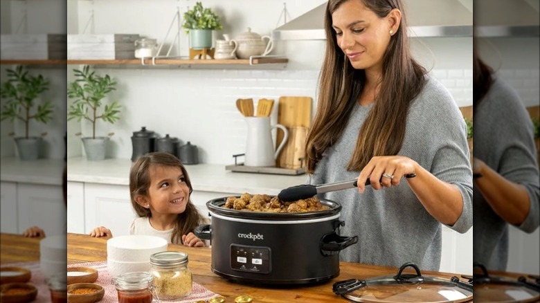 Woman using open Crock-Pot with little girl looking on