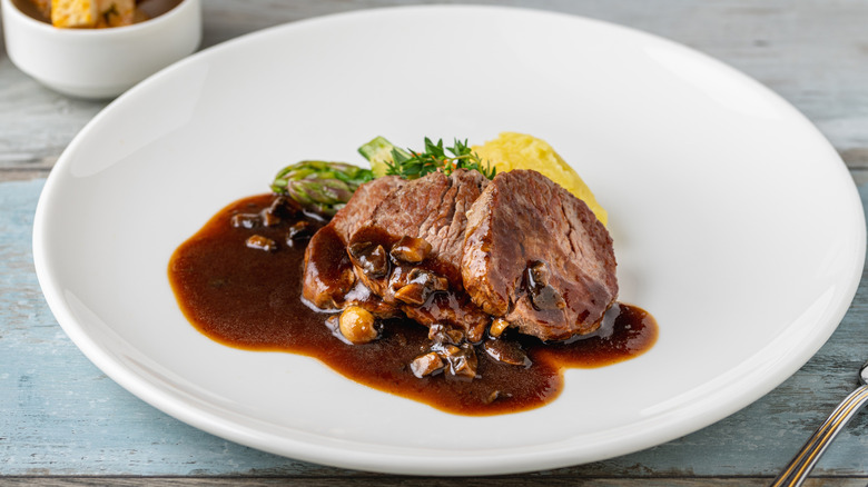 a white plate of beef tenderloin topped with espagnole sauce