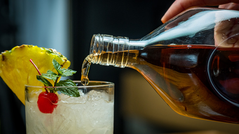 Person pouring dark liquor into a garnished cocktail