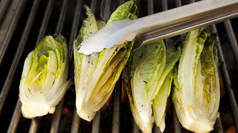 Tongs holding lettuce on grill