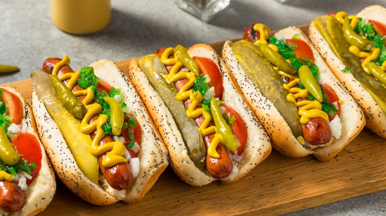 Several Chicago-style hot dogs on a wooden plank