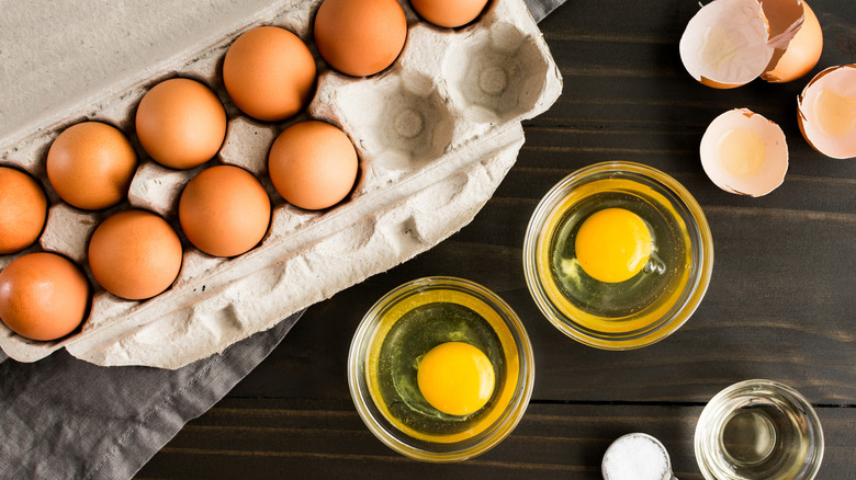 A carton of brown eggs with two cracked into small bowls.