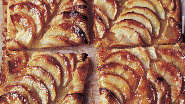 Four apple tarts on a parchment paper-lined baking sheet