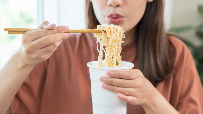 person blows on instant ramen noodles in a cup