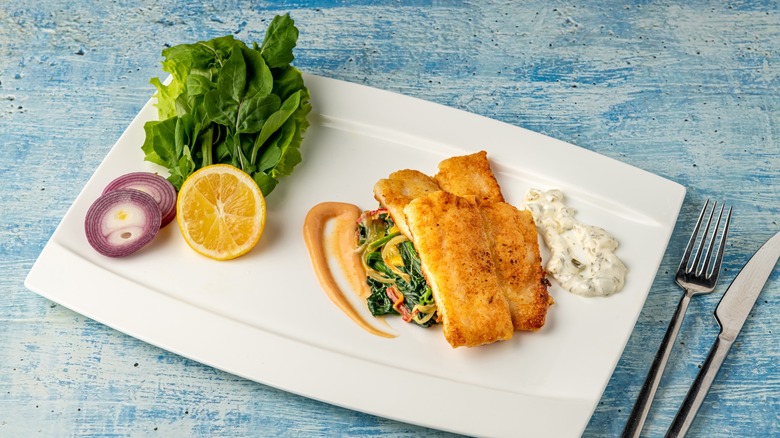 Basa fish fillet on a white plate with lettuce and veggies