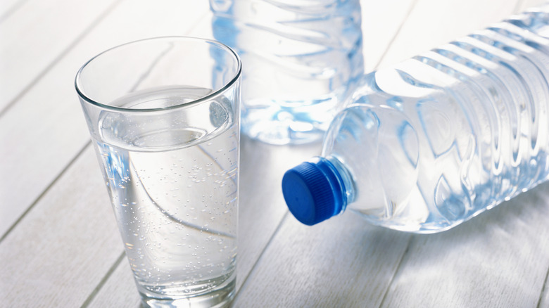 A glass of tap water sits next to two bottles of water