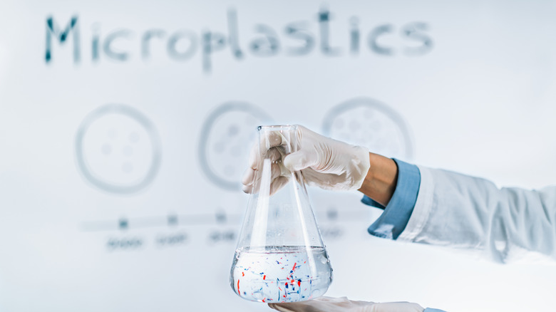 Conceptual image of a lab tech's gloved hand holding a vial of water containing microplastics