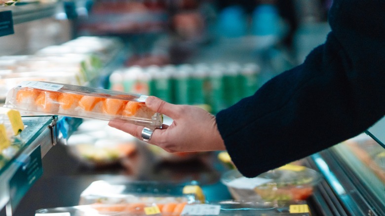 person picking up a pack of grocery store sushi