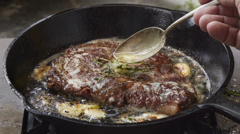 Person spooning sauce over steak cooking in a cast iron pan