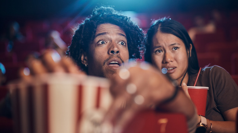 Couple hiding behind popcorn bucket while watching a movie