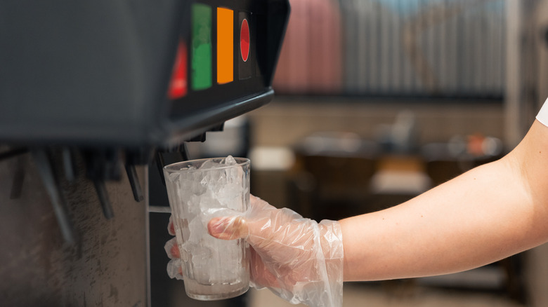 Person holding a glass with ice under a soft drink machine