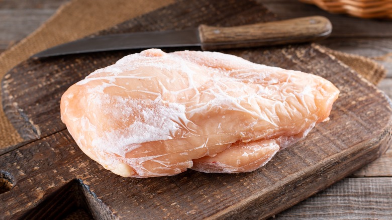 A frozen chicken breast on a wooden cutting board