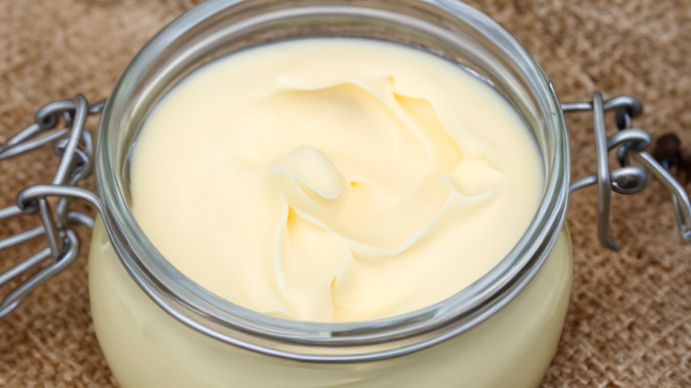 A jar of creamy homemade beef tallow sits on a scrap of burlap.