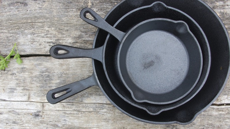 A set of cast-iron pans sits on a wooden picnic table