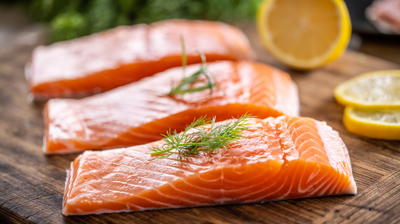 raw salmon fillets on cutting board with fresh herbs