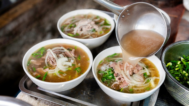 Pot pouring pho broth into three bowls of pho