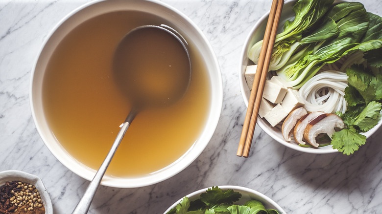 Bowl of pho broth next to bowl of ingredients