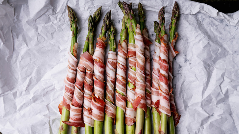 Bacon-wrapped asparagus sits on white parchment paper.