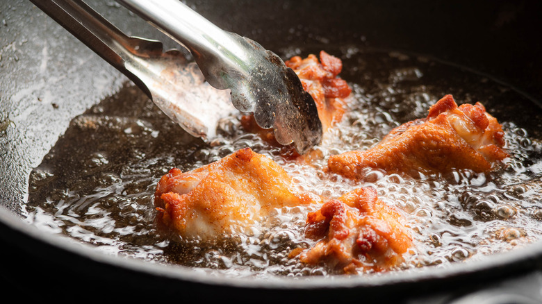 Pan frying chicken in oil with metal tongs