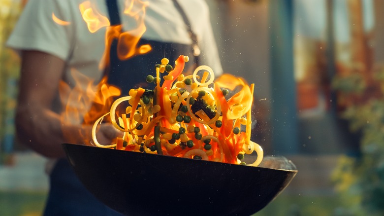 Chef tossing vegetable stir-fry in wok with flames