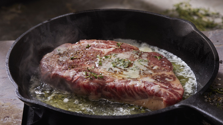 Pan searing steak in cast iron skillet with butter and seasonings