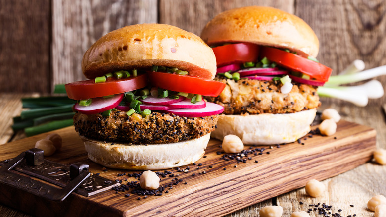 Crispy quinoa-coated veggie burgers topped with chives, tomatoes, radishes, on a wooden board