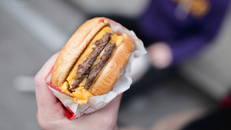 Hand holding a double cheeseburger