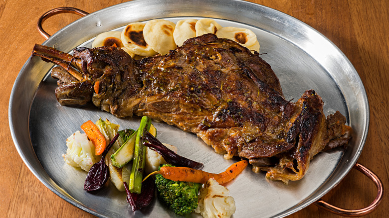 Lamb leg is displayed on a plate with vegetables.