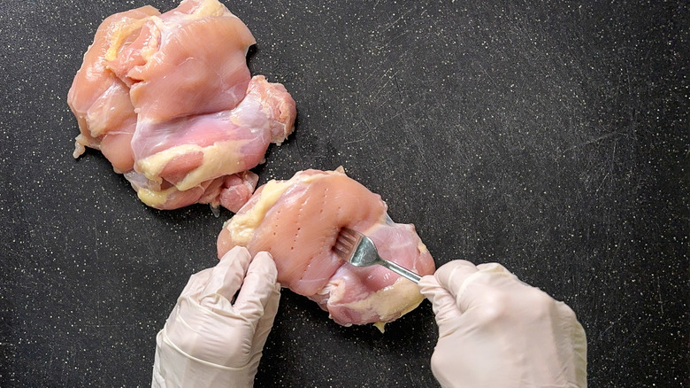 Piercing boneless skinless chicken thighs with fork on cutting board