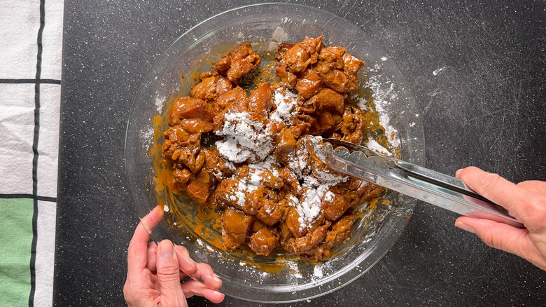 Dredging marinated chicken thighs with potato starch in pie plate with tongs