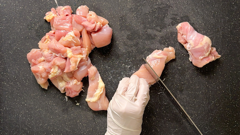 Cutting boneless skinless chicken thighs into pieces on cutting board