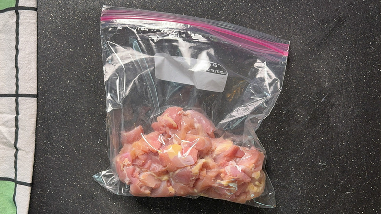 Boneless skinless chicken thigh pieces in ziplock bag on cutting board