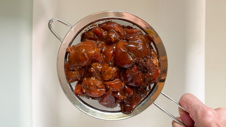 Draining excess marinade from boneless skinless chicken thigh pieces in strainer over sink