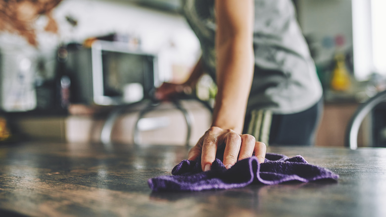 Wiping off wooden table with purple washcloth