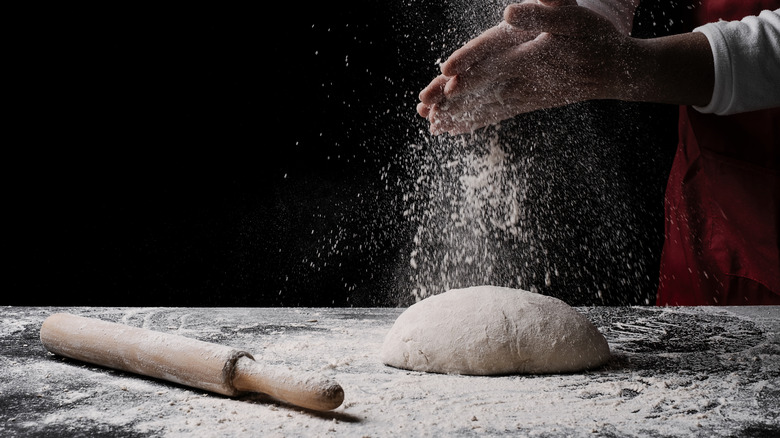 Baker's hands dusting flour onto dough alongside a rolling pin