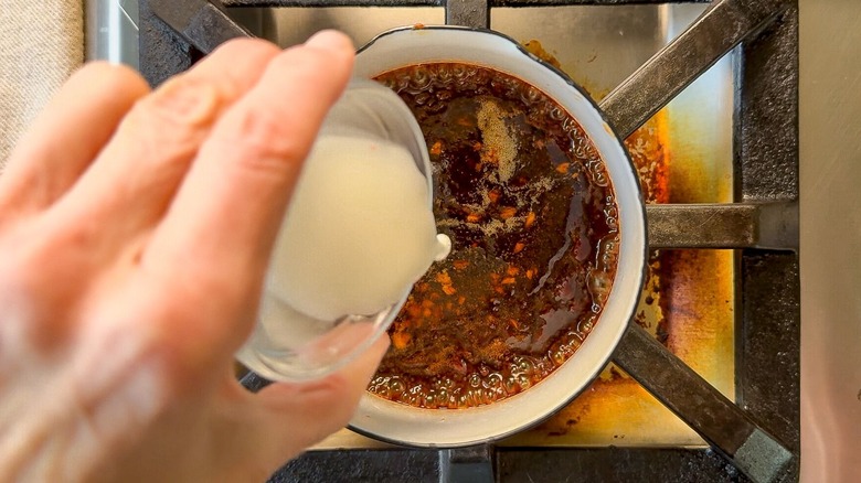 Pouring cornstarch slurry into a dipping sauce in saucepan on stovetop