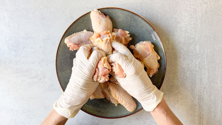 Coating chicken wings with oil wearing latex gloves