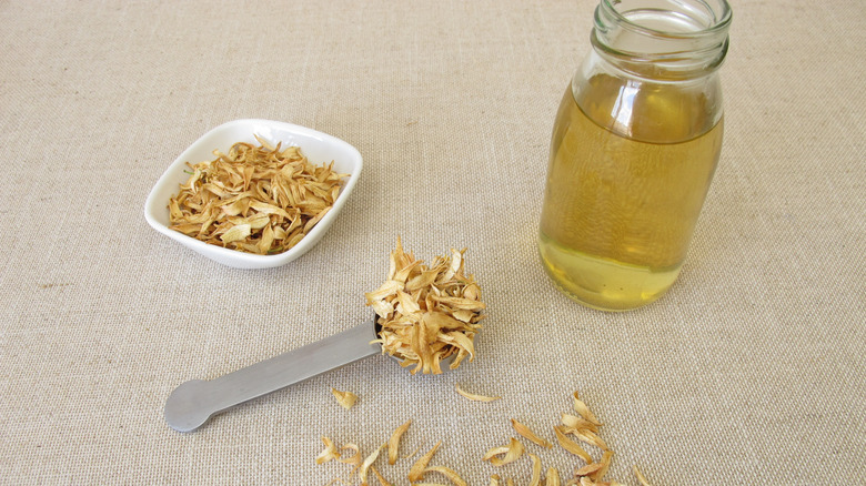 Orange blossom petals are in a dish and on a spoon next to a jar with liquid.