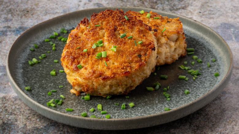 Two crispy, golden brown fish cakes on a plate covered in minced herbs