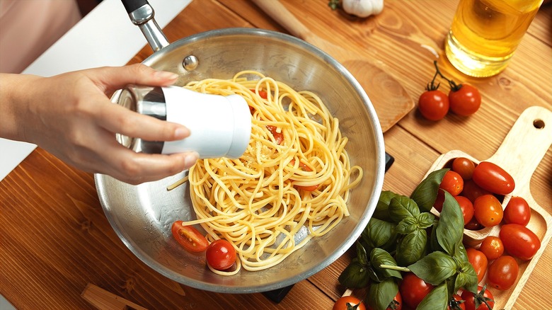 Person seasoning cooked pasta and fresh tomatoes in a steel pan