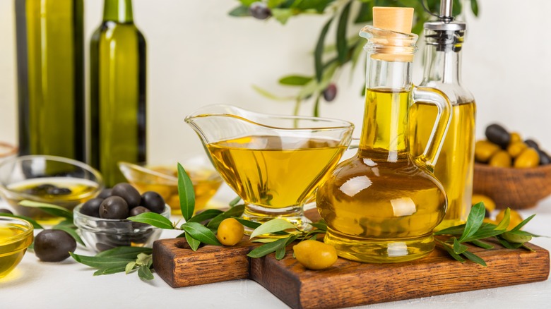 Homemade olive oil in glass jars and gravy boat on a wooden cutting board