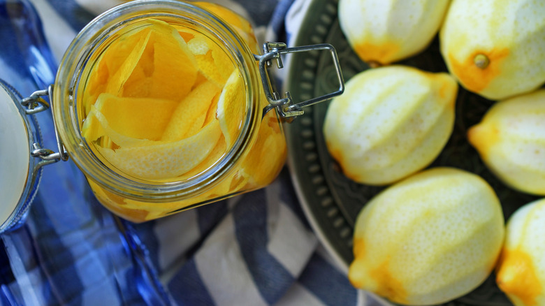 Lemon peels in a glass jar next to peeled lemons