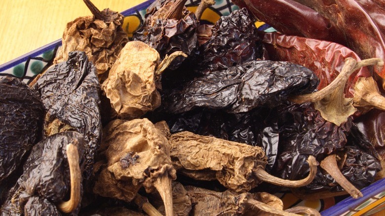 A variety of light and dark dried chiles on a ceramic platter