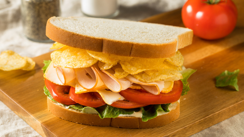 Potato chips on a turkey sandwich placed on a pretty cutting board.