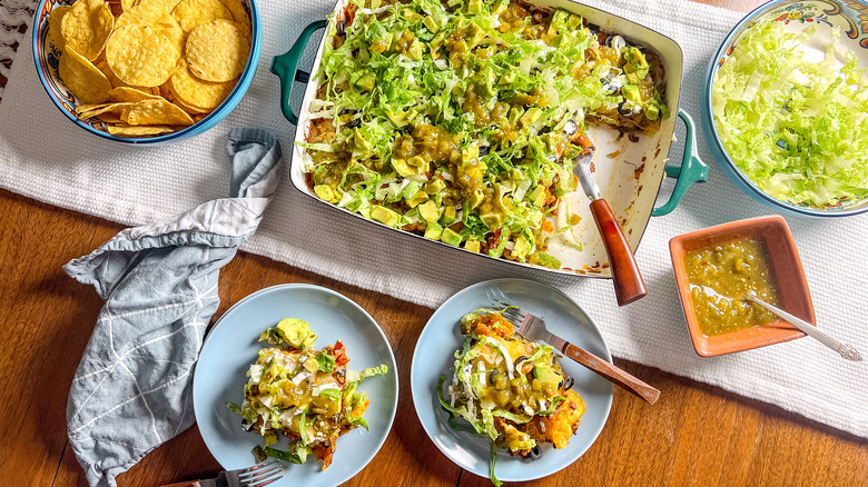 Loaded beef taco casserole in serving dish with tortilla chips and shredded lettuce and individual servings on plates