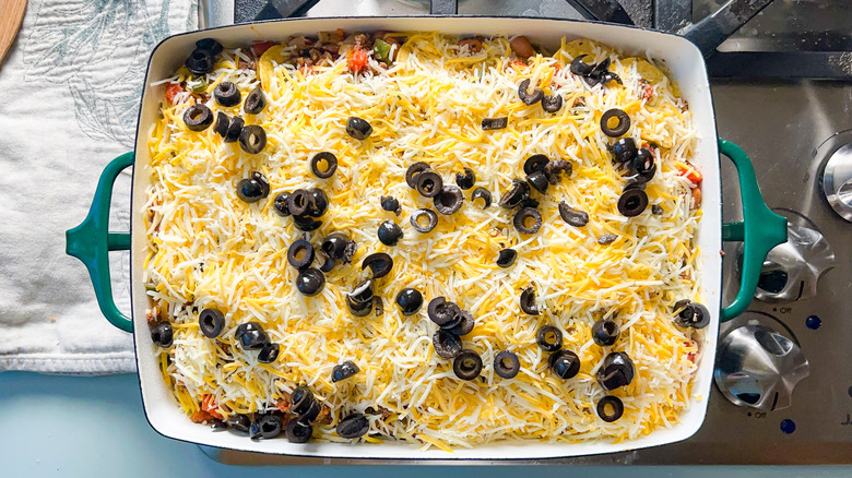 Black olives and shredded cheese on top of loaded beef taco casserole in baking pan