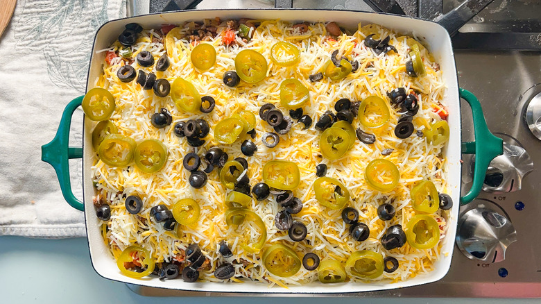 Pickled jalapenos, black olives, and shredded cheese on top of loaded beef taco casserole in baking dish